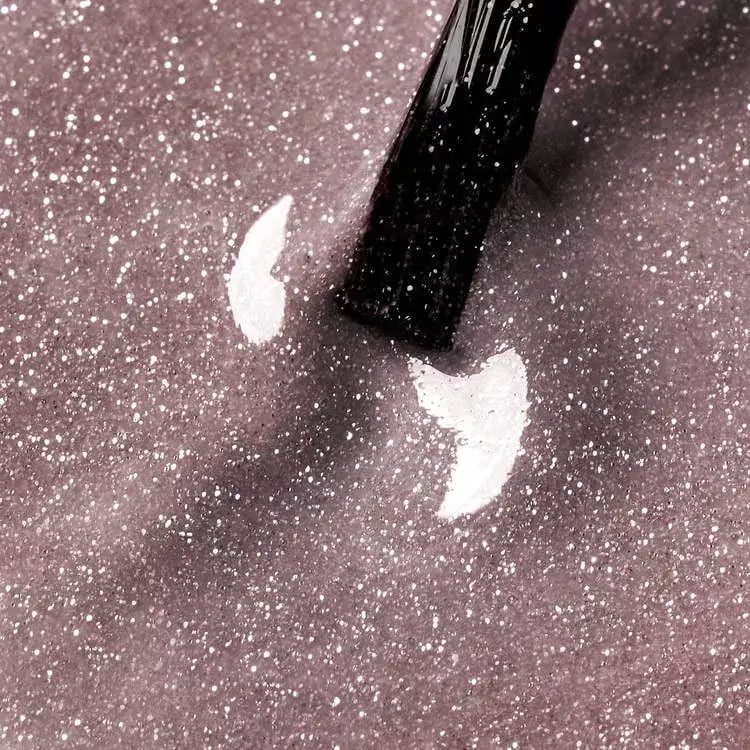 Close-up of Arctic Blush UV gel nail polish with a brush, showcasing its shimmering beige and glitter finish.