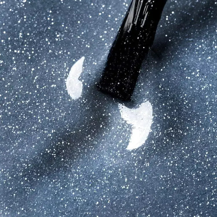 Applying Polar Sparkle UV gel polish with blue cat eye effect on a dark sparkly surface.